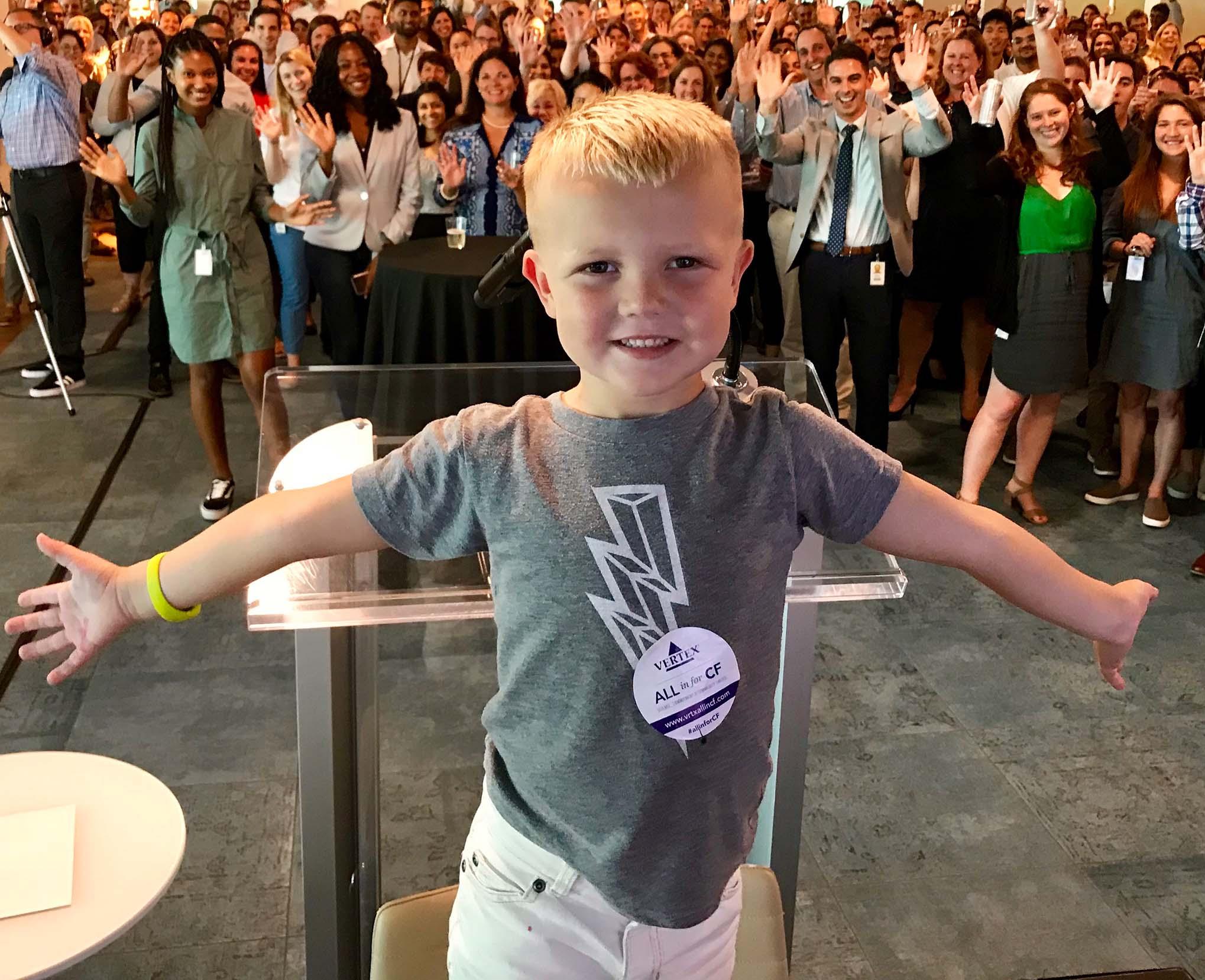 a young boy living with CF standing in front of a group of Vertex employees